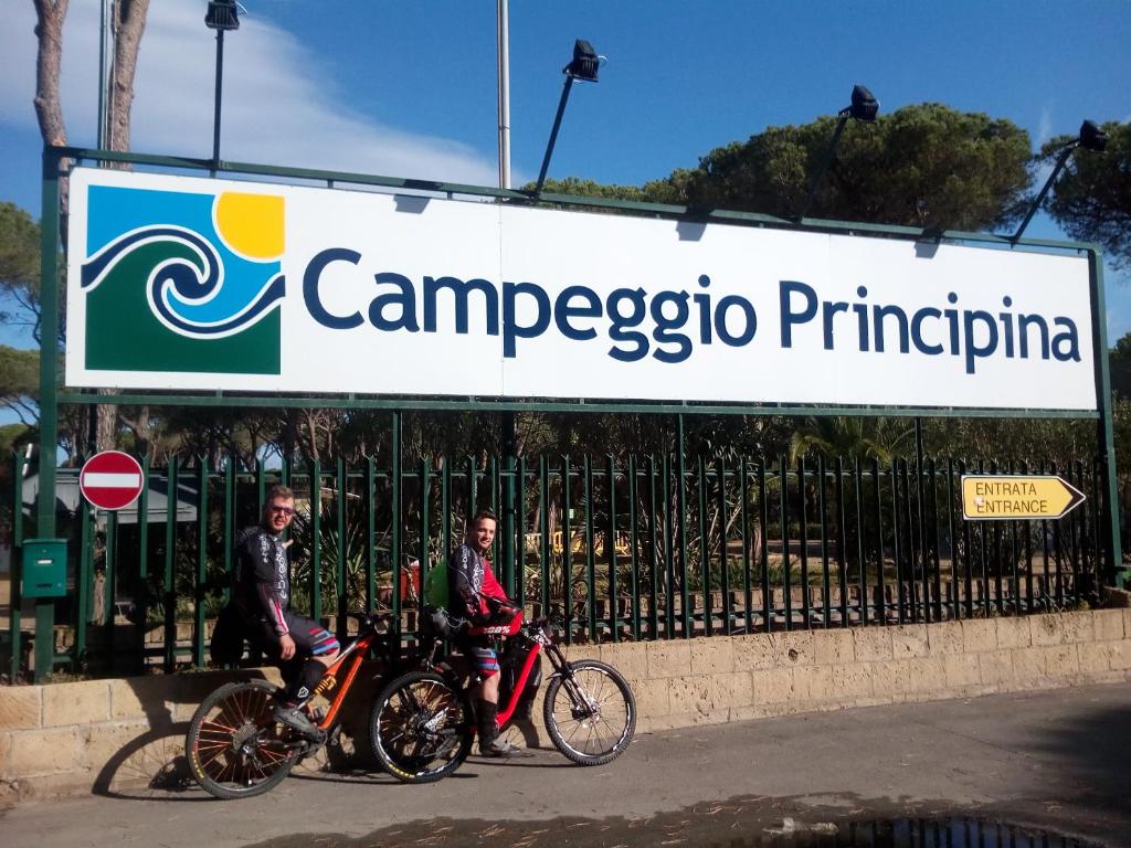 dos personas en sus bicicletas delante de una valla en Camping Principina, en Principina a Mare