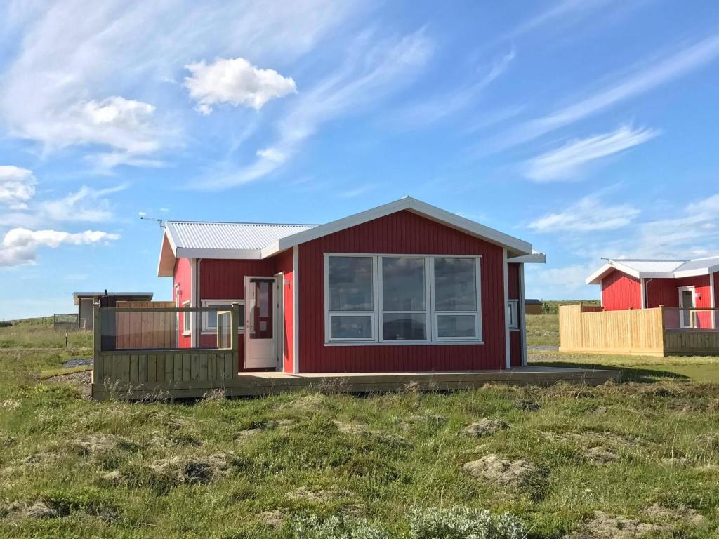 a red house on a grassy field at Blue View Cabin 1A With private hot tub in Reykholt