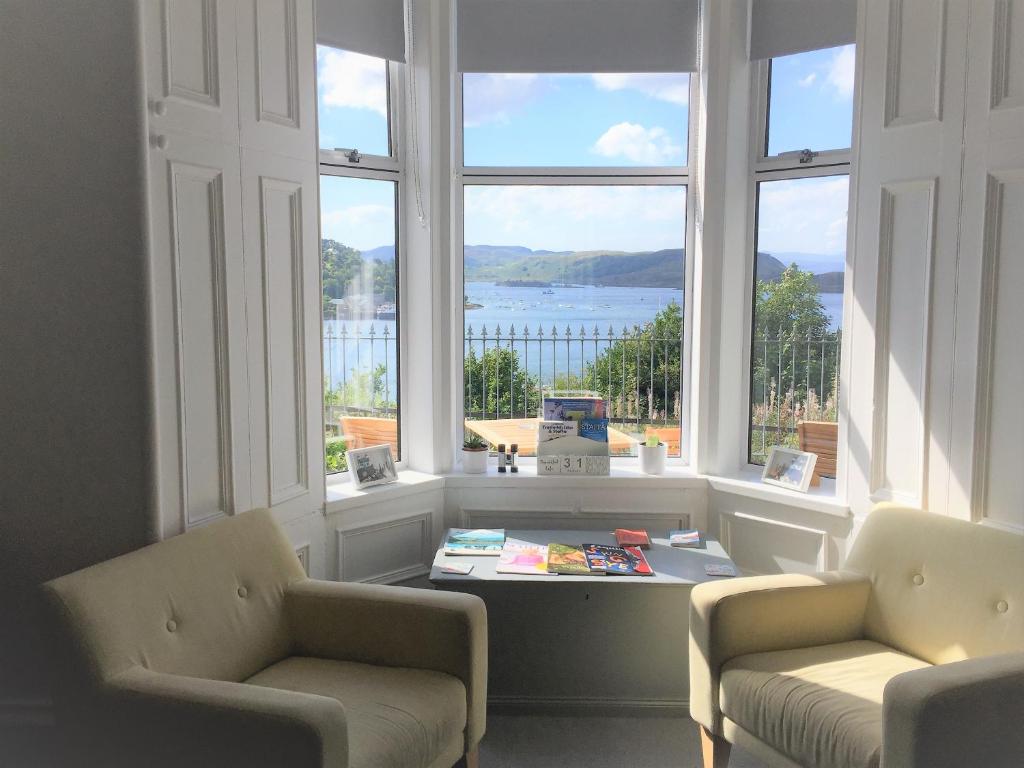 a living room with two chairs and a table and windows at Invercloy Guest House in Oban