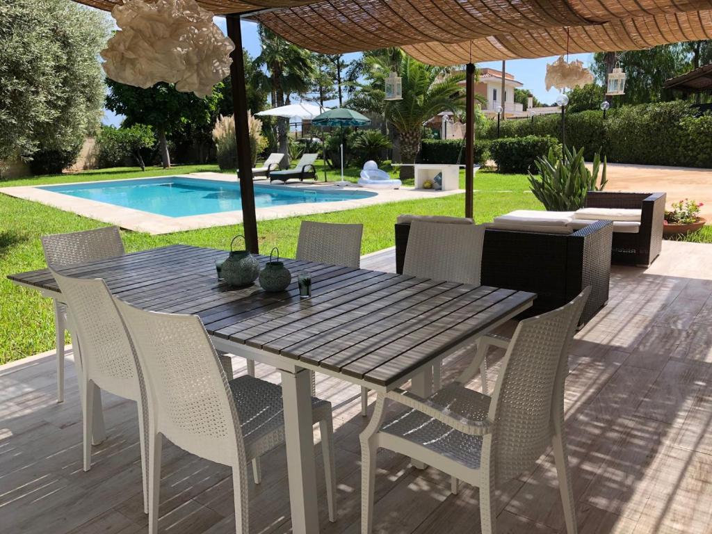 a wooden table and chairs on a patio with a pool at Villa mare Fontane Bianche in Fontane Bianche