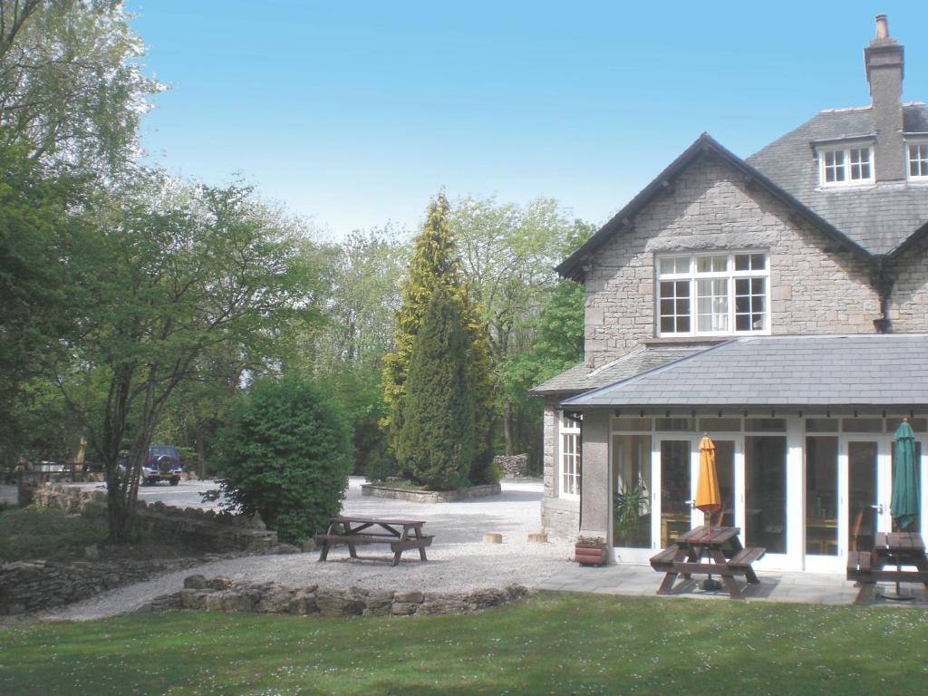una casa con mesas de picnic y bancos frente a ella en Woodlands Hotel & Pine Lodges, en Grange-over-Sands