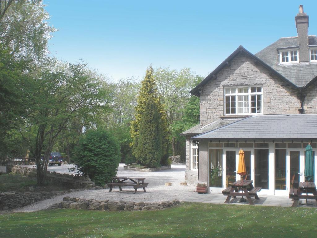 a house with picnic tables and benches in front of it at Woodlands Hotel & Pine Lodges in Grange Over Sands