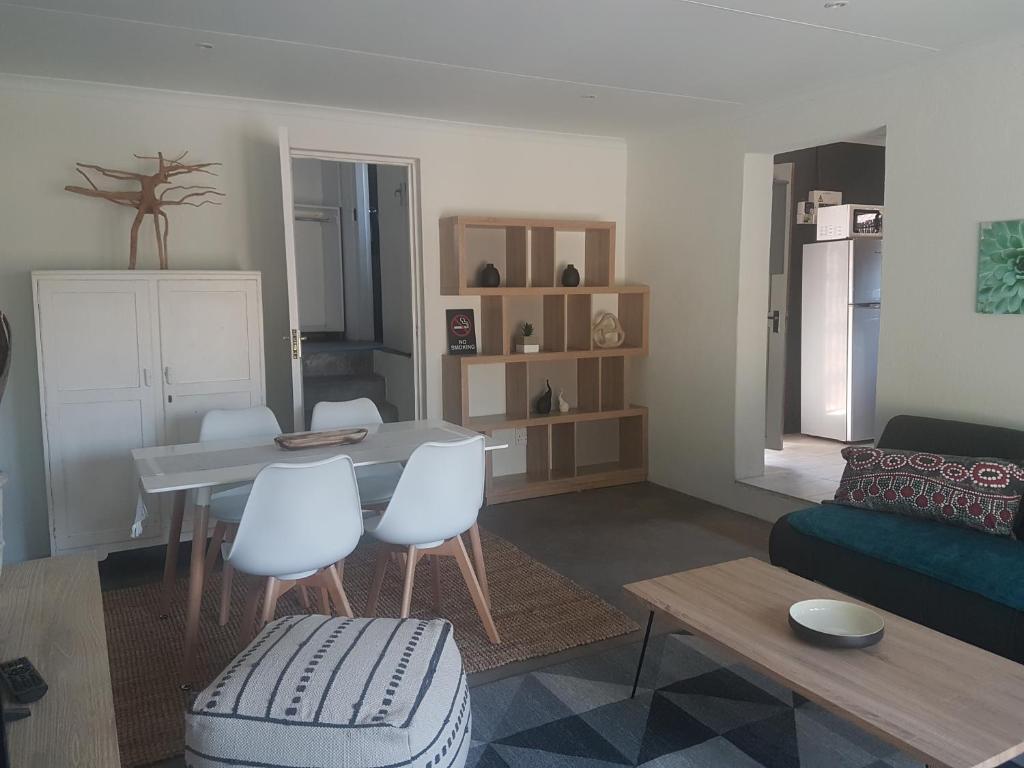 ein Wohnzimmer mit einem Tisch und weißen Stühlen in der Unterkunft Tangled Tree Cottage in Roodepoort