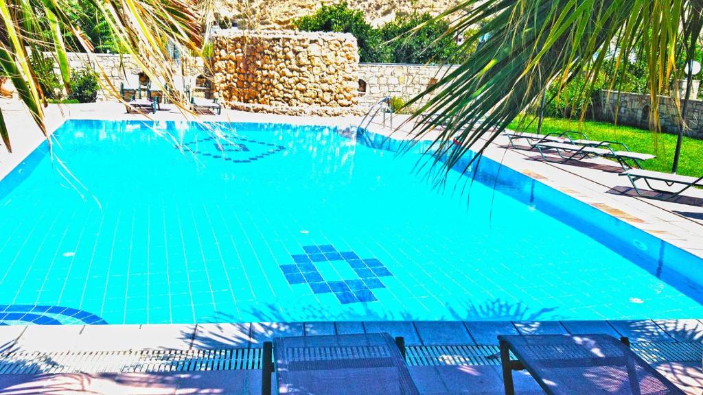 a blue swimming pool with chairs and a palm tree at Dimitris Villa Hotel in Matala