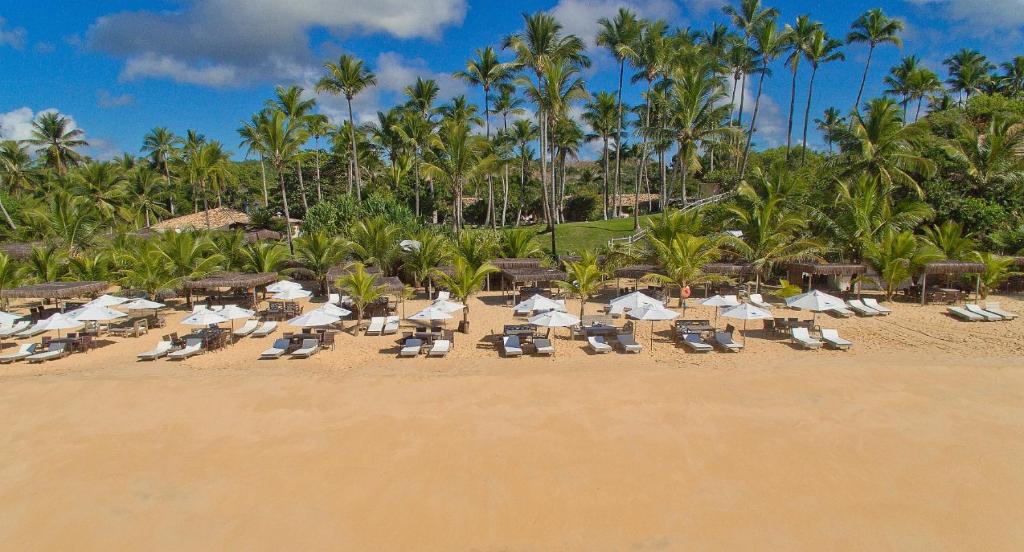 a beach with chairs and umbrellas and palm trees at Rio Da Barra Villa Hotel in Trancoso