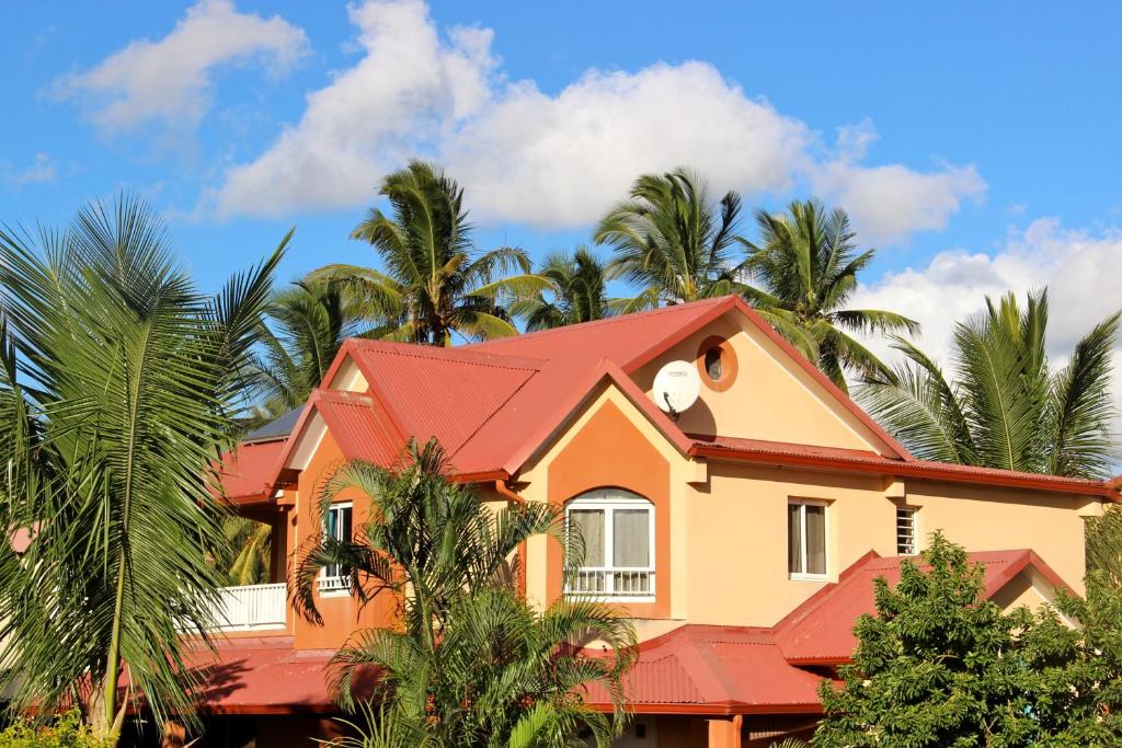 une maison avec un toit rouge et des palmiers dans l'établissement La Kaz à l'Étang - Votre Location de Vacances à l'Île de La Réunion, à Saint-Louis