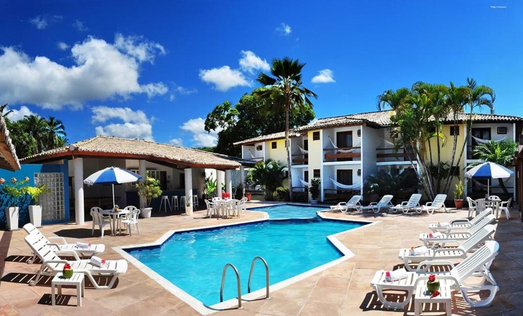 a resort with a swimming pool and chairs and a building at Hotel Oceano Porto in Porto Seguro