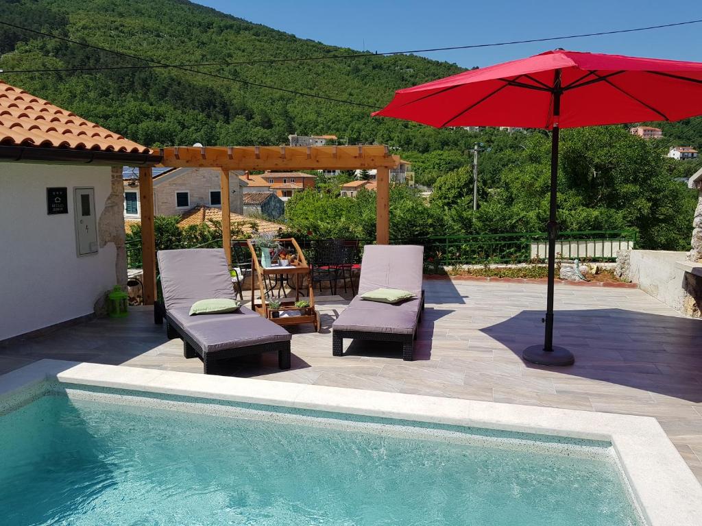 einen Pool mit 2 Stühlen und einem roten Regenschirm in der Unterkunft Diana Holiday Home in Brseč