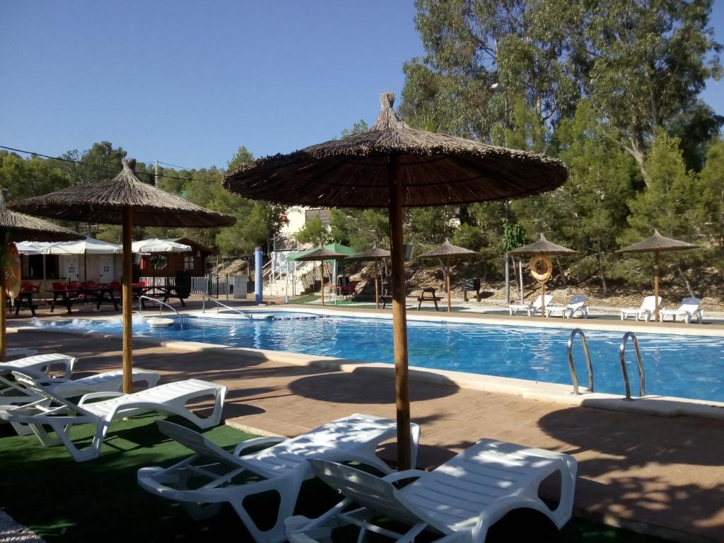 a swimming pool with chairs and umbrellas and a swimming pool at Camping la Pedrera in Bigastro