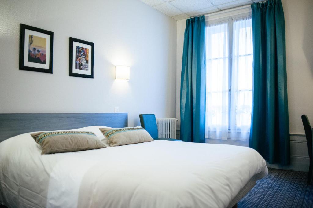 a bedroom with a white bed with blue curtains and a window at Hôtel Carmin in Le Havre