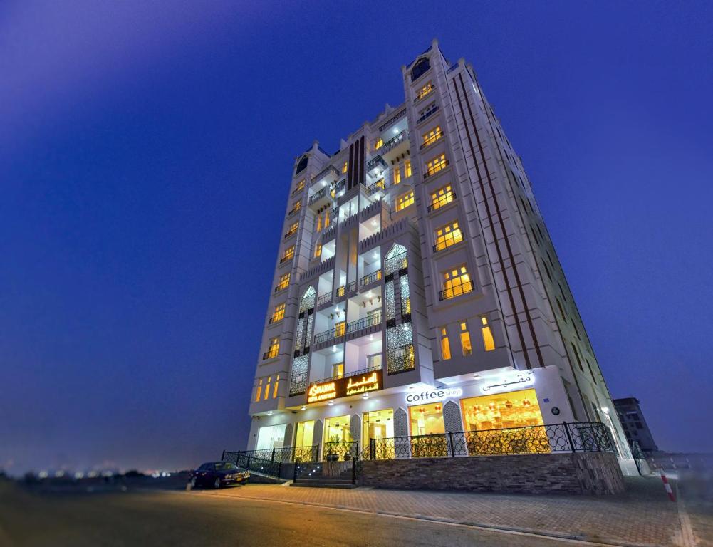 een hoog gebouw met veel ramen 's nachts bij A'Sinamar Hotel Apartment in Muscat