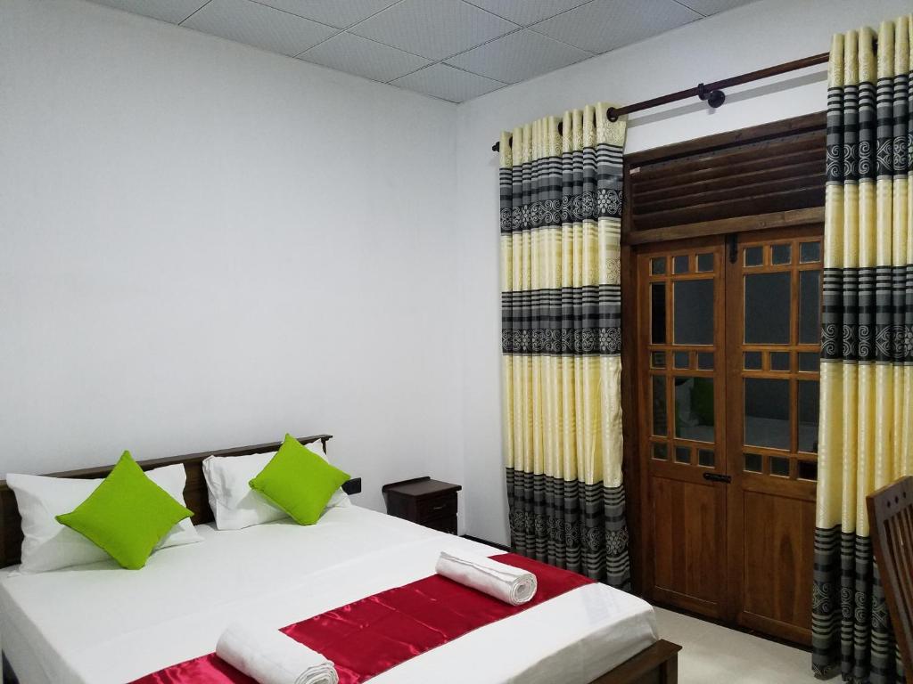 1 dormitorio con 1 cama con almohadas verdes y rojas en Yashumi Homestay, en Dambulla