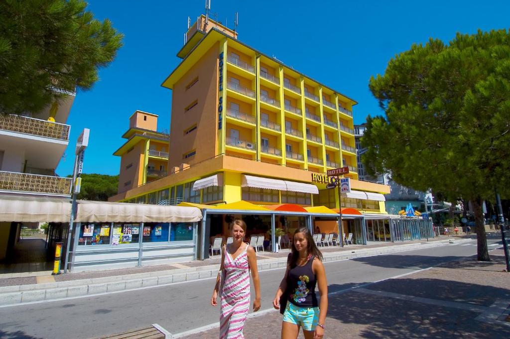 Due donne che camminano per una strada davanti a un edificio giallo di Hotel Sole a Rosolina Mare