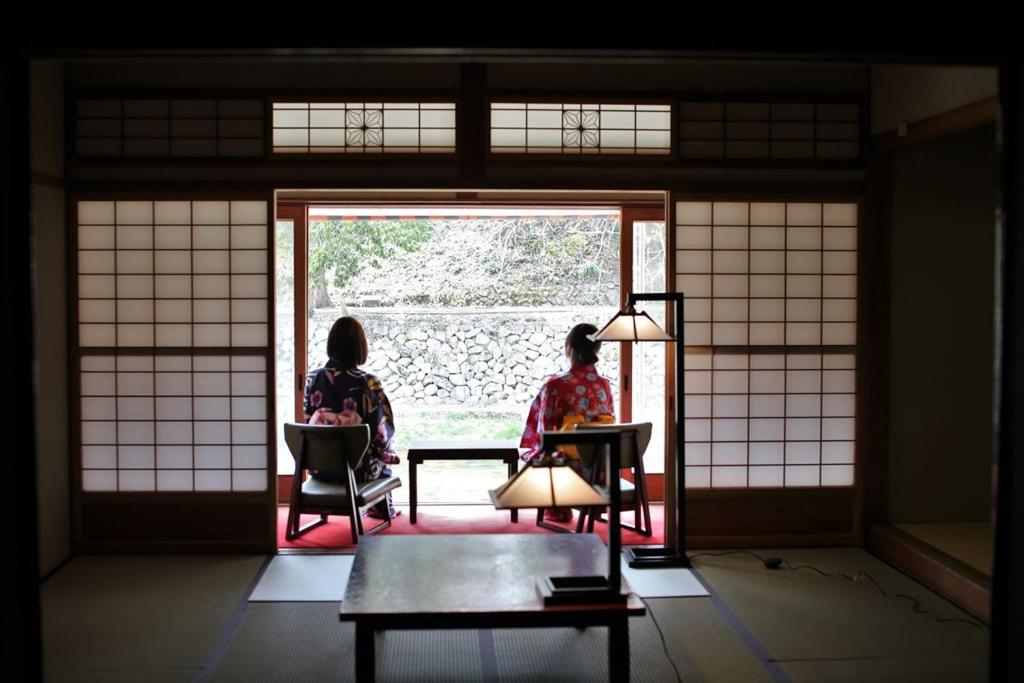 Kagamino的住宿－OkutsuHotSpa IkedayaKajikaen，坐在椅子上,看着窗外的两名妇女