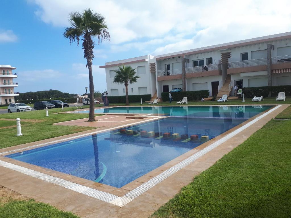 a swimming pool in front of a building with a palm tree at Résidence Dreamland in Sidi Rahal