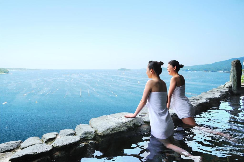 Dos mujeres están de pie sobre una roca en el agua en Minami Sanriku Hotel kanyo en Shizugawa