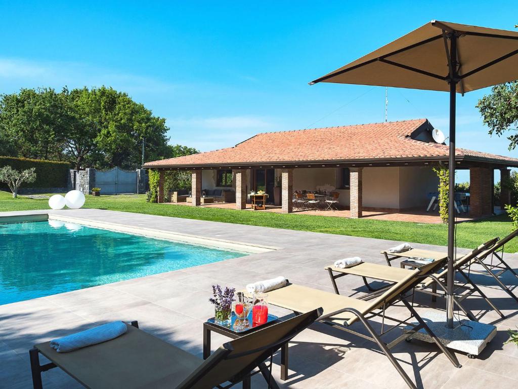 a pool with chairs and an umbrella next to a house at Belvilla by OYO Viagrande in Trecastagni