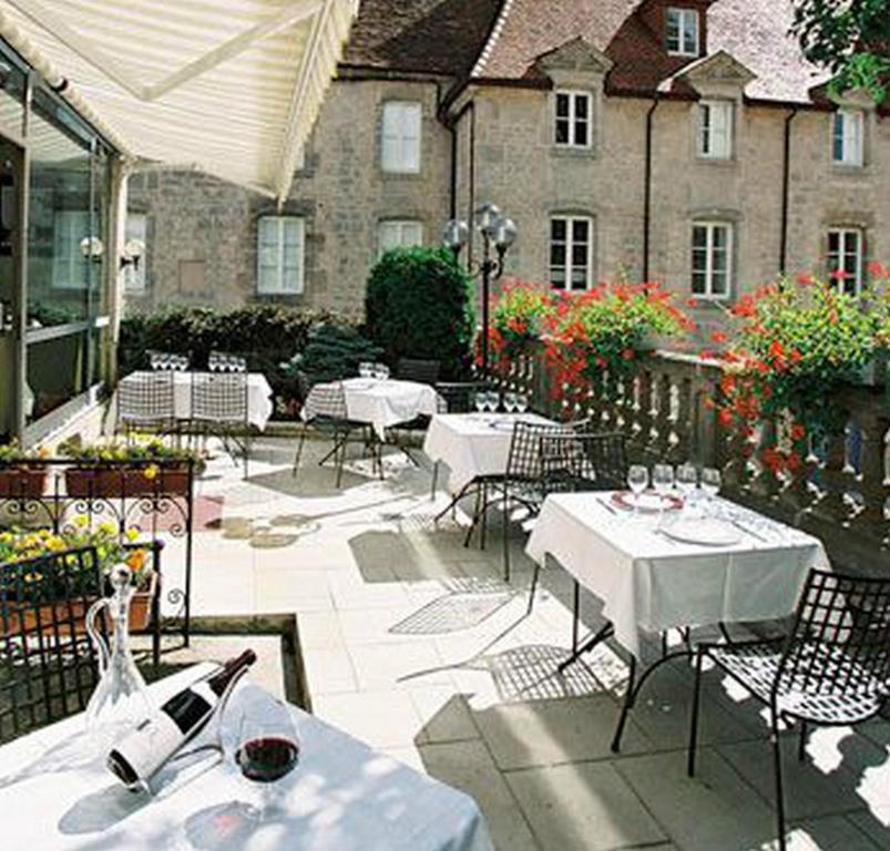 um pátio com mesas e cadeiras brancas e um edifício em Logis Hôtel Le Cheval Blanc em Langres