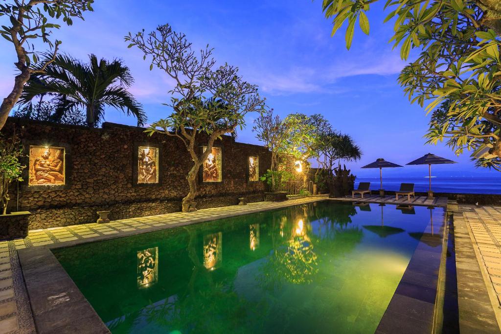 a swimming pool in front of a house with the ocean at Alam Candi Dive Resort in Candidasa