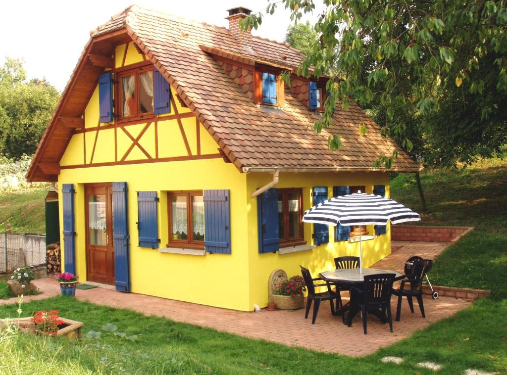 ein gelbes Haus mit einem Tisch, Stühlen und einem Regenschirm in der Unterkunft Gite en Alsace in Mutzig