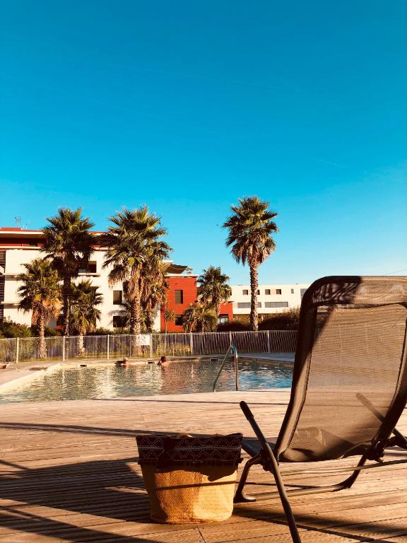 une chaise assise à côté d'une piscine bordée de palmiers dans l'établissement Appartement 1 ROYAL VILLEROY, à Sète