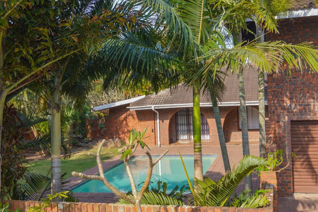 a house with a swimming pool between two palm trees at Emangunini Guest house in Richards Bay