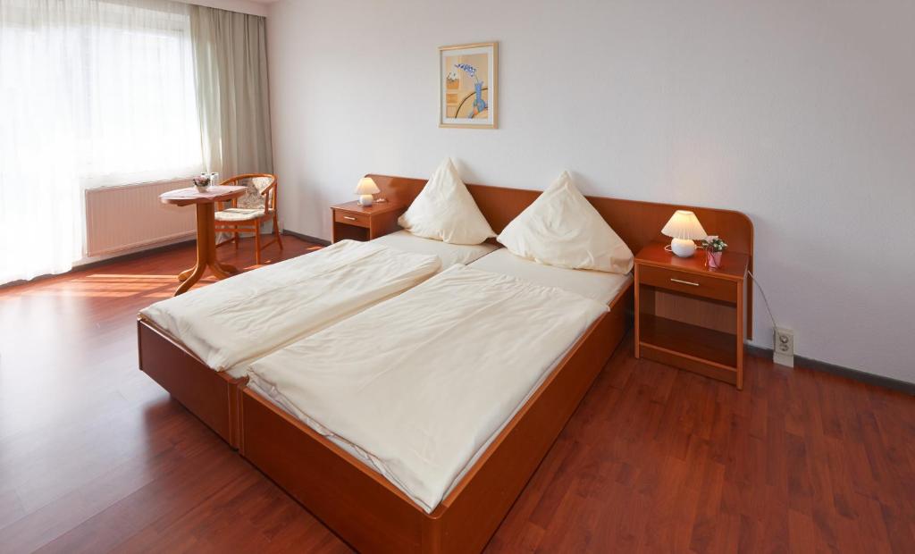 a bedroom with a large bed with white sheets and wooden floors at Alpha Apparthotel leipzig-Rötha in Rötha