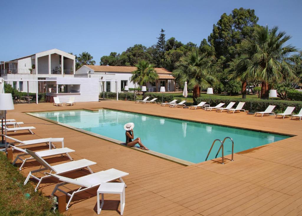a person sitting next to a swimming pool with lounge chairs at Il Vigneto Resort in Menfi