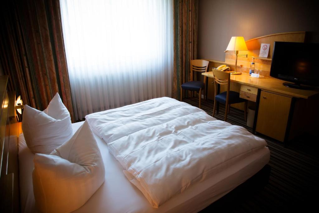 a bedroom with a bed and a desk and a window at Rheinhessen Inn GmbH in Wörrstadt