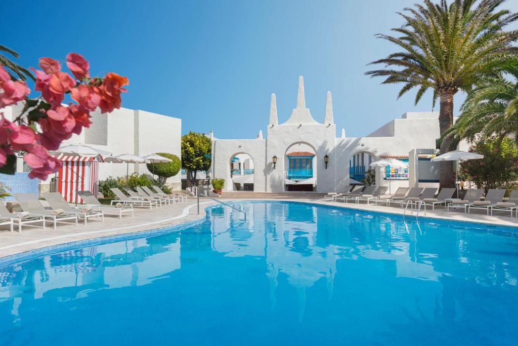 a swimming pool in front of a house with a church at Alua Suites Fuerteventura in Corralejo