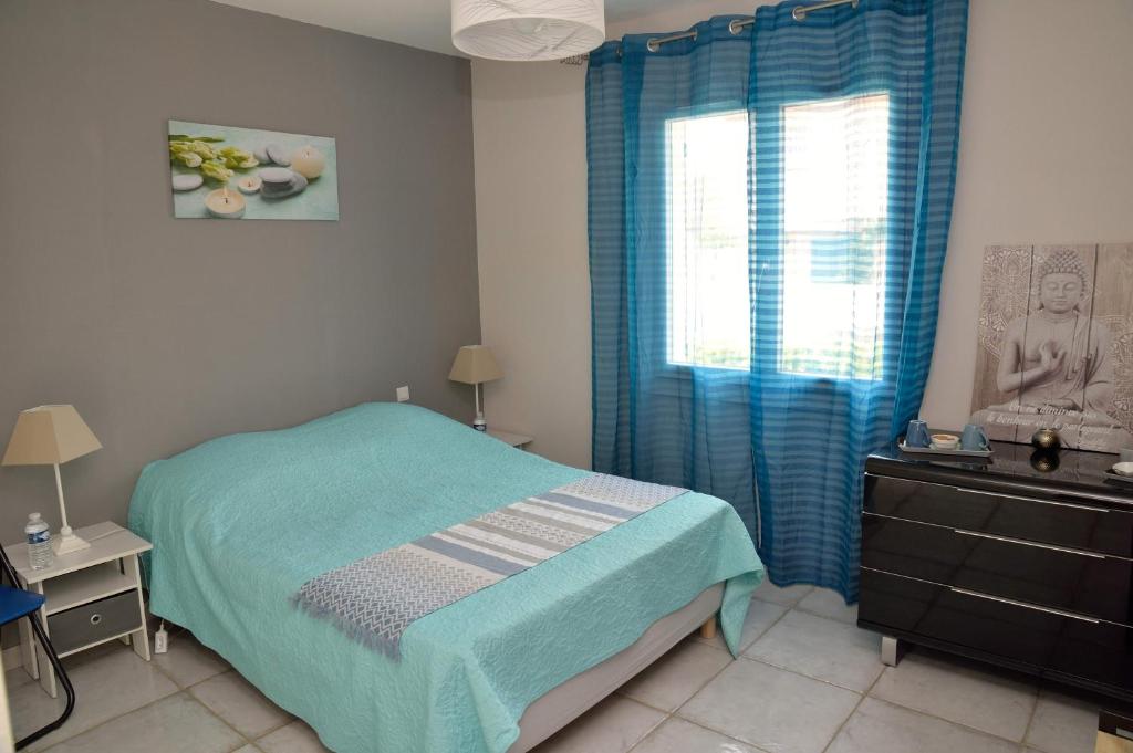 Schlafzimmer mit einem Bett und einem Fenster mit blauen Vorhängen in der Unterkunft Les Amandiers in Abeilhan