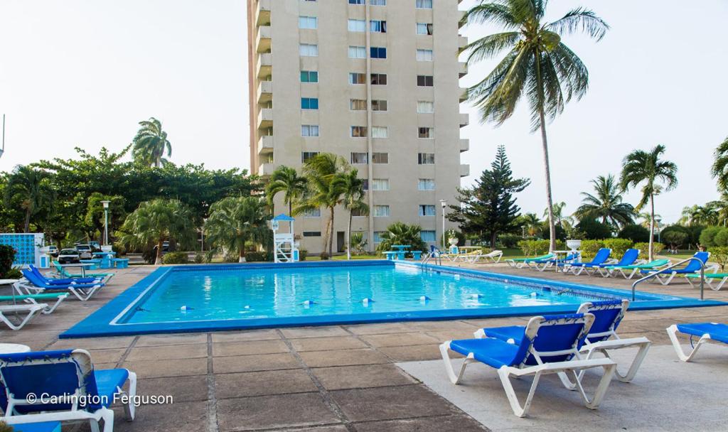 einem großen Pool mit blauen Stühlen und einem Gebäude in der Unterkunft Sword Fish Beach Suite@ Turtle Towers in Ocho Rios
