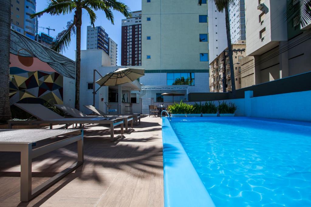 a swimming pool with lounge chairs and an umbrella at Santa Inn Hotel in Balneário Camboriú