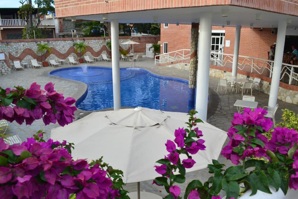 una sombrilla blanca y flores púrpuras junto a una piscina en Hotel Villa Playa Grande en Playa Grande