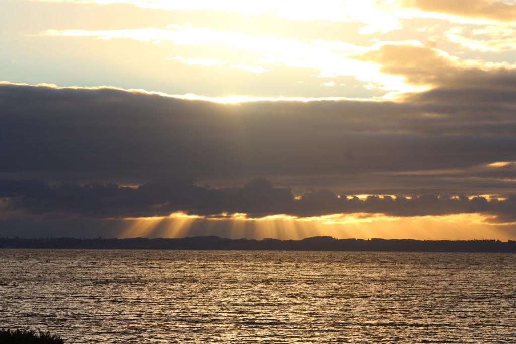 una puesta de sol sobre un cuerpo de agua con el sol brillando en Cabañas Ruta Del Lago, en Puerto Varas