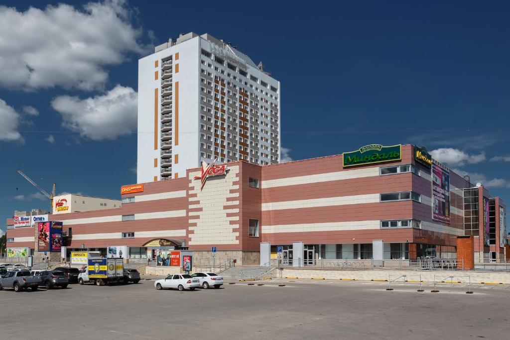 un gran edificio con coches estacionados en un estacionamiento en Vega Hotel, en Tolyatti