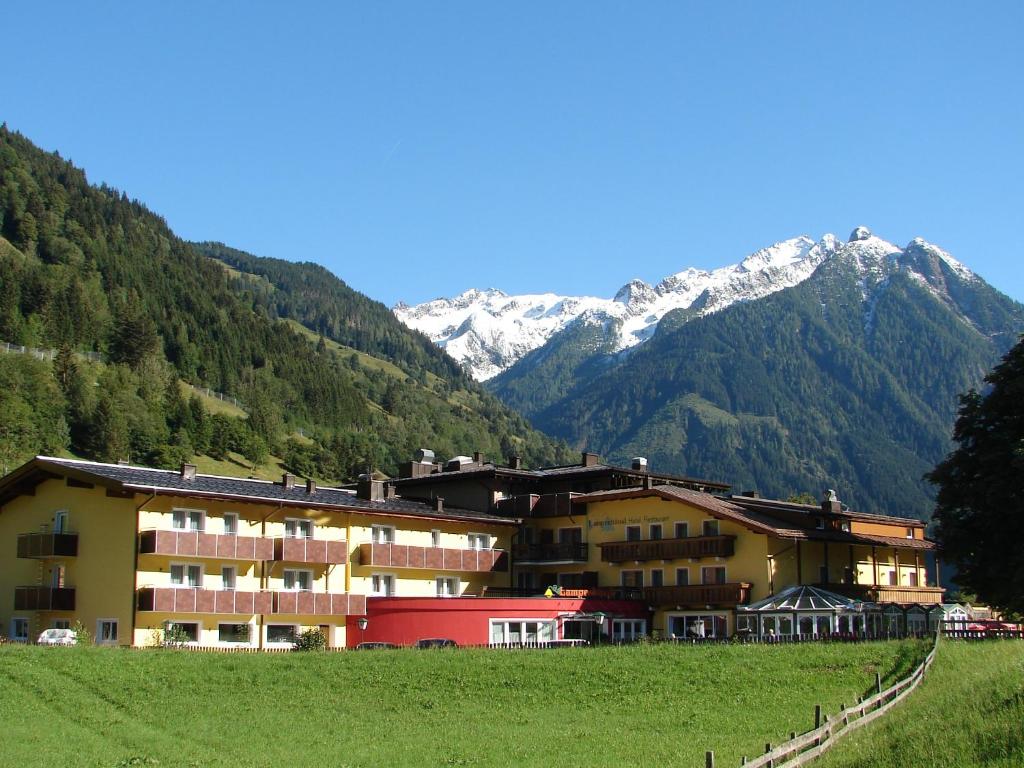 a building in a field with mountains in the background at Hotel-Restaurant Lampenhäusl in Fusch an der Glocknerstraße