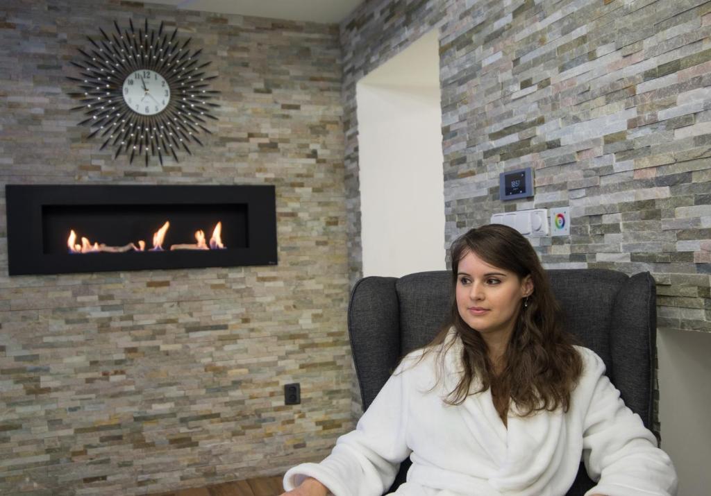 a woman sitting in a chair in front of a fireplace at Wellness Apartmán Relax in Český Těšín