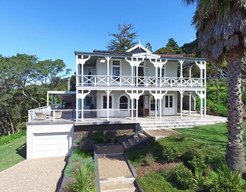 a large white house with a porch and a palm tree at The Sanctuary- Stay Waiheke in Oneroa