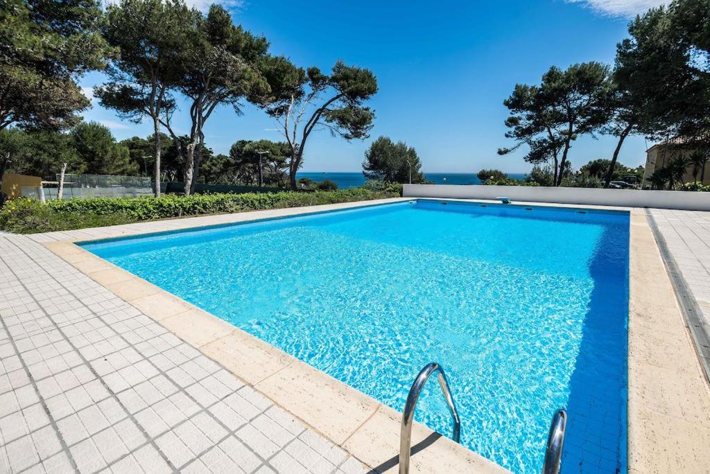 a blue swimming pool with trees and the ocean in the background at Seafront Unit 2 in Cascais