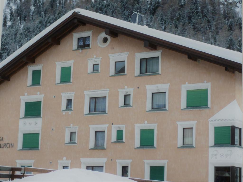 un bâtiment avec des fenêtres vertes et blanches et une montagne dans l'établissement Curtins 16, à Pontresina