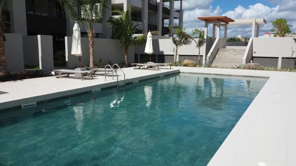 una piscina con 2 sillas y un edificio en Element Bay Lux Beach Apartment, en Cap Malheureux