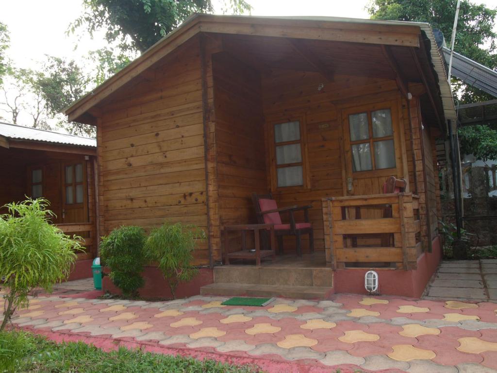 Cabaña de madera pequeña con porche y 2 sillas en Santonio Resorts, en Anjuna