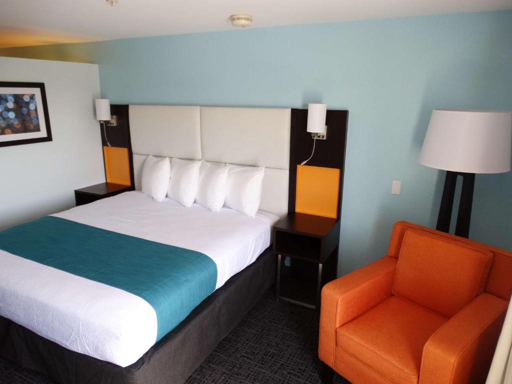 a hotel room with a bed and an orange chair at Best Western Plus Orlando Lake Buena Vista South Inn & Suites in Kissimmee