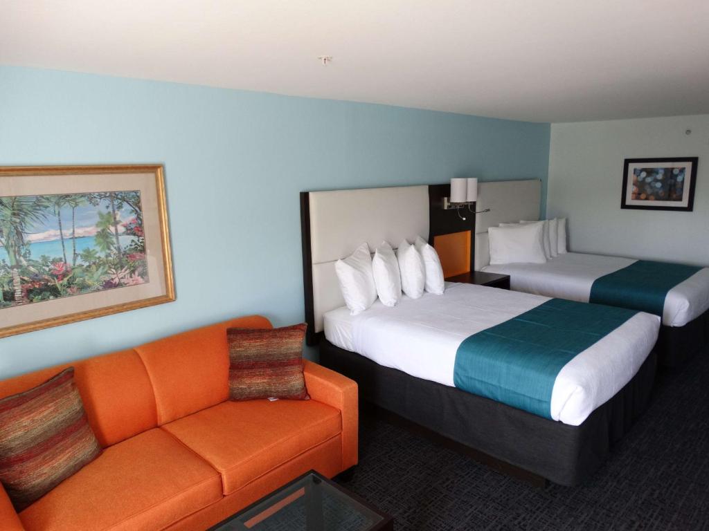 a hotel room with two beds and an orange couch at Best Western Plus Orlando Lake Buena Vista South Inn & Suites in Kissimmee