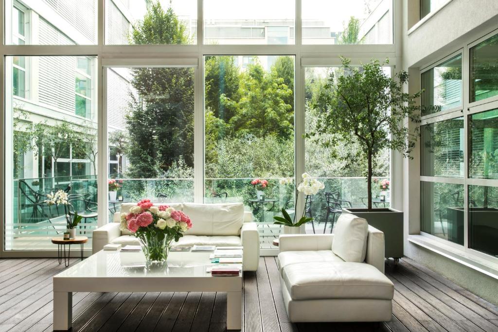 una sala de estar con muebles blancos y ventanas grandes. en Magna Pars l'Hotel à Parfum, en Milán