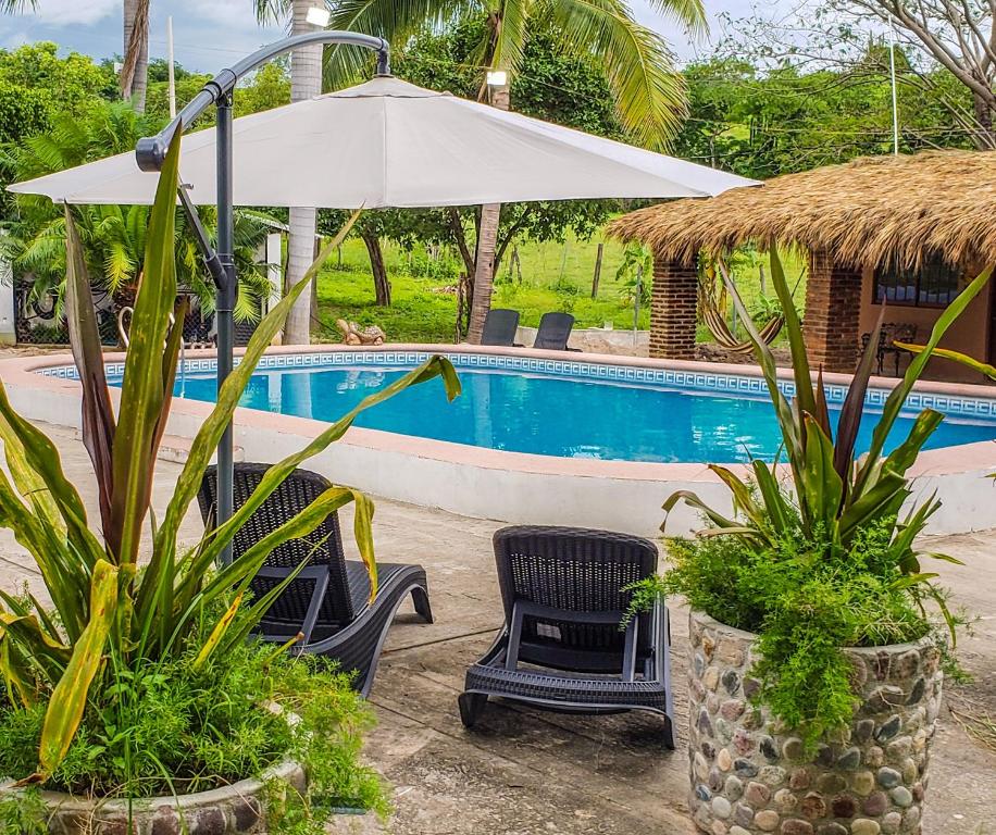 a swimming pool with two chairs and an umbrella at Cabañas El Potrero in Cosalá