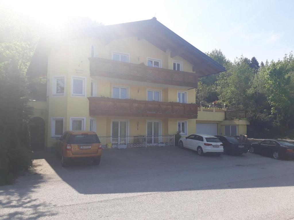 une grande maison jaune avec des voitures garées dans un parking dans l'établissement Apartment Sonnblick, à Sankt Johann im Pongau