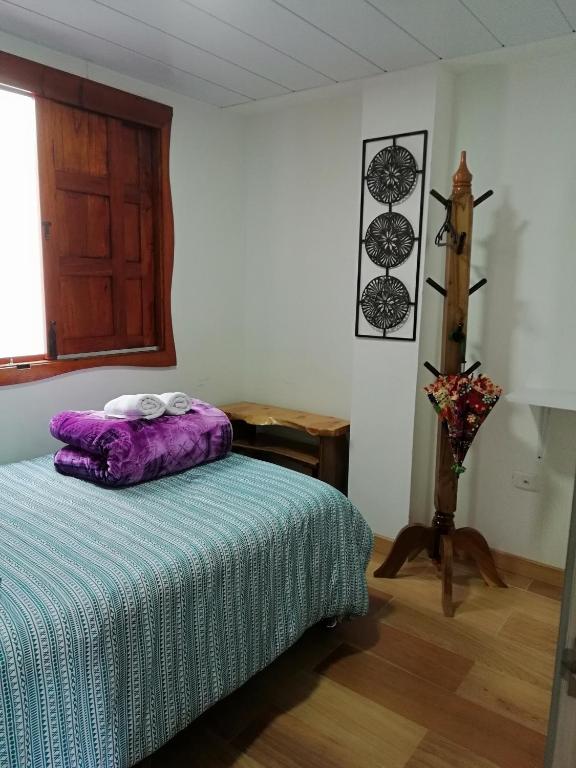 a bedroom with a bed with a purple comforter and a window at Elizabetha Hostal in Salento