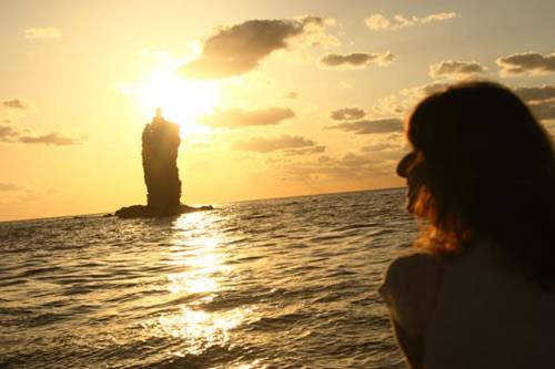 una mujer de pie en la playa mirando la puesta de sol en Okinoshima Resort Island Park Hotel, en Tsudo